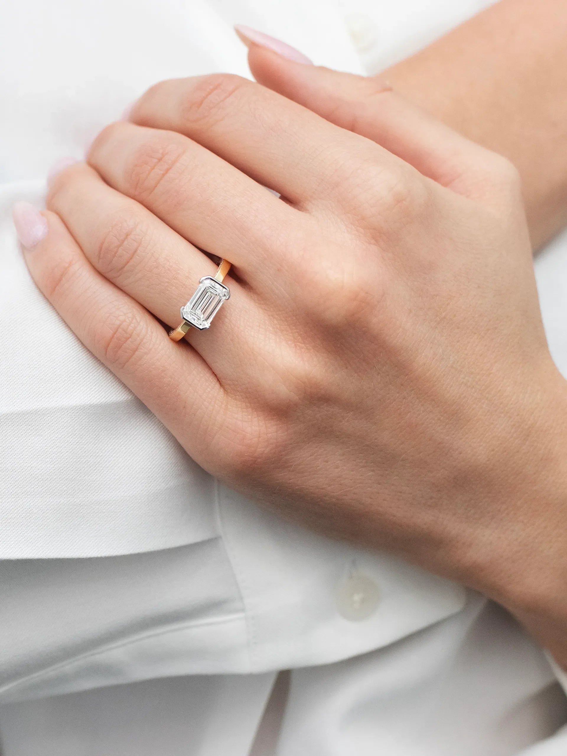 East-west emerald solitaire with a half bezel and single-sided diamond band.